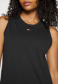 Top senza maniche nero realizzato in morbido tessuto, con scollo rotondo e un piccolo logo in rosso e bianco sul lato sinistro del petto.