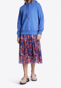 Sudadera azul con un corte holgado, combinada con una falda con varias capas, colorida y con estampado. Zuecos rosas con tachuelas completan el conjunto.