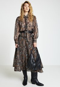 Paisley-patterned, black and brown long dress with cuffs, belted waist, and flowy skirt. Black fringed handbag and cowboy boots complete the look.