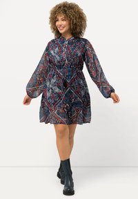 Mekko, jossa pitkät hihat ja polvimittainen pituus, valmistettu läpinäkyvästä kankaasta. Kuviointi on paisley-tyyliä sinisissä, punaisissa ja kermanvärisissä sävyissä. Mekossa on vyötäröä korostava leikkaus ja pyöreä pääntie.
