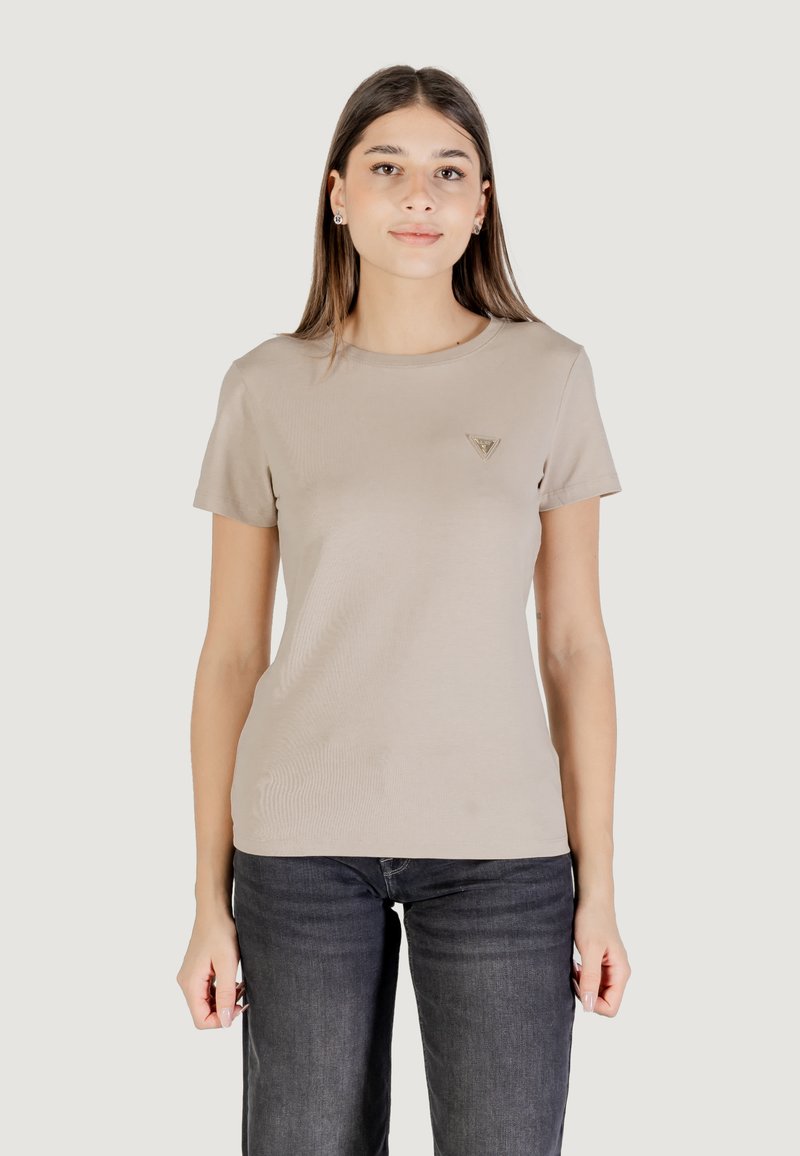T-shirt aderente beige con maniche corte, scollatura rotonda e un piccolo logo triangolare sul lato sinistro del petto. Abbinato a jeans di denim scuri.
