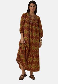 Robe maxi en rouille avec un motif en diamant vert et jaune. Présente un encolure froncée et des manches amples. Accentuée par des fentes latérales et un tissu superposé.