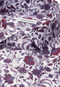 Chemise en coton blanche avec des motifs floraux violets et rouges, avec des boutons blancs et une étiquette portant la mention "seidensticker" à l’intérieur du col.