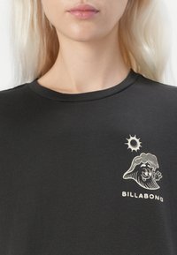 Black cotton t-shirt featuring a graphic design of a wave character and sun in cream at the left chest area. Round neckline, short sleeves.
