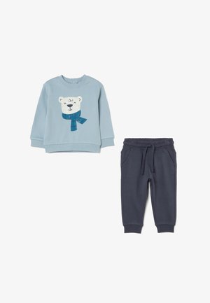 Felpa azzurra chiara con grafica di un orso polare e una sciarpa blu, abbinata a pantaloni morbidi blu navy con vita elastica.