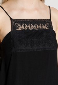 Camisola nera con spalline sottili, caratterizzata da un pannello in pizzo ricamato nella zona del petto. Tessuto leggero, morbido e design in semplice nero.
