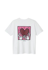 T-shirt en coton blanc avec un design graphique au dos : deux figures stylisées soulevant un cœur marron sur un fond rose.