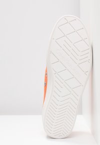 Orange canvas-sneaker med vit gummisula, med ett texturerat mönster på sulan och Calvin Klein Jeans-varumärke på undersidan.