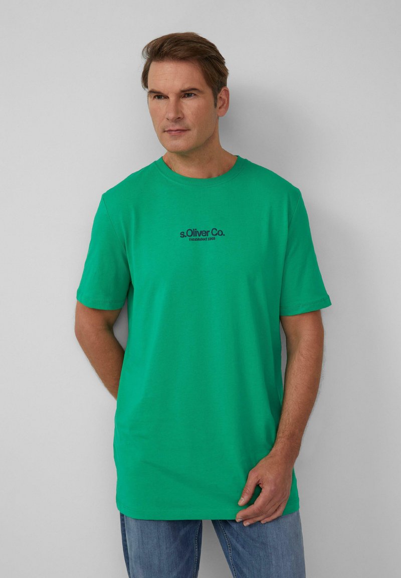 Zielona bawełniana koszulka z krótkimi rękawami, okrągłym dekoltem i czarnym nadrukowanym logo "s.Oliver Co. Established 1969" na wysokości klatki piersiowej.
