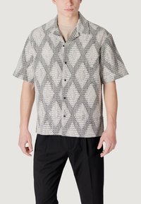 Camicia a maniche corte con un motivo a rombi in bianco e nero, dotata di chiusura con bottoni e tessuto textured. Indossata sopra pantaloni neri.