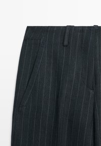 Donkergrijze geruite broek met ceintuurlussen en schuin aangebrachte frontzakken, getoond van taille tot halverwege het dijbeen.