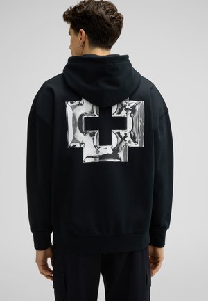 Zwarte hoodie met een groot, glanzend metallic kruisontwerp op de achterkant. Gemaakt van zachte stof met een capuchon met trekkoord en geribbelde manchetten.