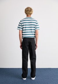 Striped teal and white cotton T-shirt paired with black pants. The T-shirt features short sleeves and a relaxed fit; pants have side pockets.