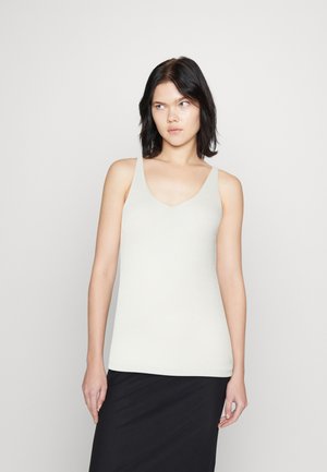 Ribbed, light beige tank top with a V-neckline and wide straps, made of a soft textured material. Paired with a black skirt.