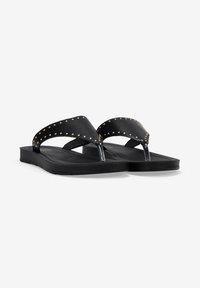 Flip-flop neri con cinturini borchiati, realizzati in un materiale simile alla gomma. Presentano una suola piatta e un accento metallico tra le dita.