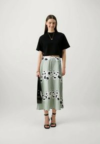 Naisel on seljas must lühendatud t-särk, helesinine midi-seelik musta ja valge lillemustriga, mustad kõrged kontsad ja käes must käekott.