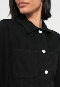 Μαύρο τζιν μπουφάν με γιακά, ασημί κουμπιά τύπου snap και δύο τσέπες στο στήθος με λεπτή υφή.