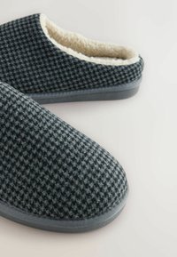 Gray plaid slippers with a soft lining, featuring a rounded toe and a smooth rubber sole. The upper material has a fuzzy texture.
