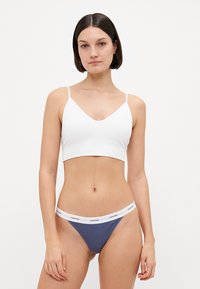 Brassière en coton blanc avec bretelles ajustables associée à un string côtelé bleu avec une taille blanche portant la mention "Calvin Klein."