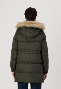 Olīvu zaļš pūkains mētelis ar mākslīgās kažokādas apdari uz kapuces, quiltēta dizaina, garām piedurknēm un spiedpogu aprocēm.