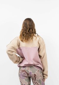 Fleece sweatshirt in lichtbeige en roze met een relaxte pasvorm; gecombineerd met gestreepte leggings met bloem en abstracte ontwerpen in gedempte kleuren.