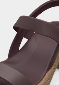 Κοντινό πλάνο ενός καφέ σανδαλιού με δύο πλατιές λουράκια και σόλα σε στυλ πλεγμένης εσπαντρίγιας.