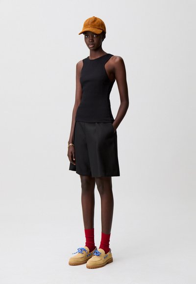 Top negro sin mangas, pantalones cortos negros con bolsillos, zapatos beige claro con cordones azules y una gorra marrón. Diseño sencillo, textura suave.