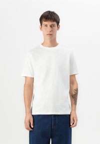 T-shirt en coton blanc à manches courtes, col rond, coupe décontractée, texture lisse. Porté avec un jean en denim bleu.