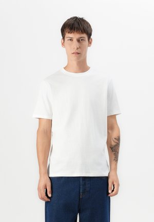 Weißes Baumwoll-T-Shirt mit kurzen Ärmeln, Rundhalsausschnitt, lockerer Passform und glatter Textur. Getragen mit blauen Jeans.