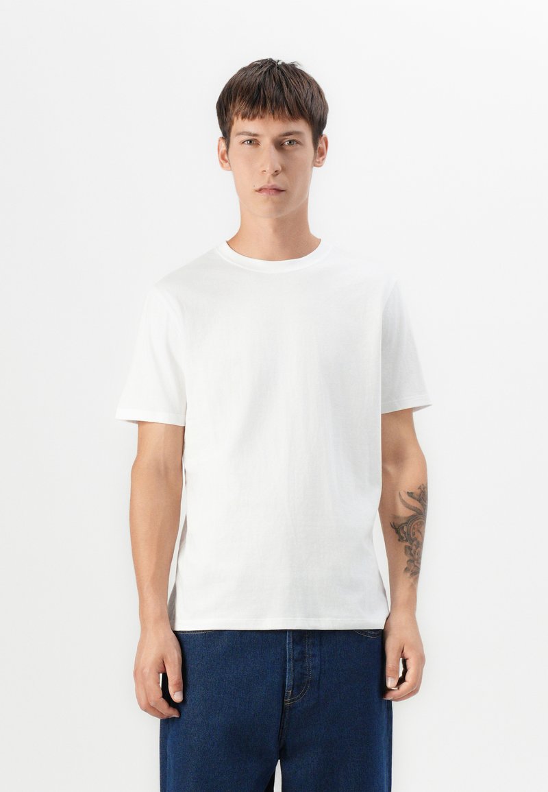 T-shirt en coton blanc à manches courtes, col rond, coupe décontractée, texture lisse. Porté avec un jean en denim bleu.
