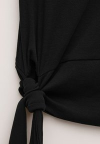 Musta kangas, joka on solmittu yksinkertaisella solmulla vaaleaa taustaa vasten ja näyttää kankaan rakenteen ja laskokset.