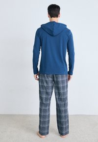 Langemouwige blauwe hoodie met een achterzak, gecombineerd met gestreepte grijze pyjamabroek, met een relaxte pasvorm en zachte stof.