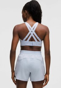 Sujetador deportivo azul claro con tirantes entrelazados y una cinturilla ligera. Pantalones cortos de tela cómoda con bolsillos, a juego en color.