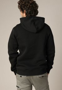 Zwarte hoodie met een trekkoordcapuchon, textuurstof, en geribbelde manchetten en zoom. Gemaakt met lichtgrijze cargobroek.