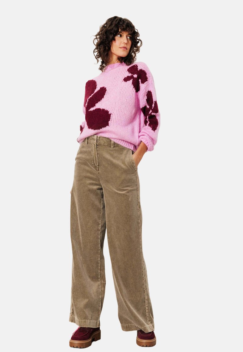 Pull en tricot rose avec des motifs floraux bordeaux, associé à un pantalon large en velours côtelé beige et des chaussures à plateforme bordeaux.