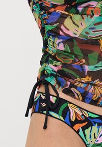 Biquíni multicolorido com um top franzido apresentando padrões de folhas verdes, rosas e azuis; parte de baixo preta com design floral a condizer e laços ajustáveis.