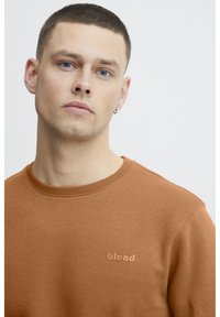 Sudadera marrón con cuello redondo, tejido texturizado y un sutil logo "blend" en un tono más claro. Diseño sencillo y ajuste casual.