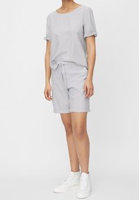 Haut à manches courtes rayé avec taille nouée et short assorti. Tissu doux, couleurs gris clair et blanc, et revers de manches roulées. Baskets blanches.