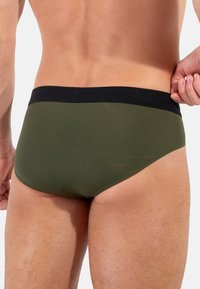 Oliwkowe slipy kąpielowe z czarnym elastycznym pasem w talii. Gładka tekstura i dopasowany krój podkreślający kontury ciała.