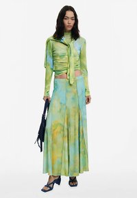 Grønt og blåt tie-dye sæt med en tætsiddende top med bindebånd foran og et løstsiddende, plisseret skørt. Båret med blå sandaler med stropper.