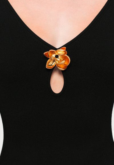Black ribbed bodysuit featuring a deep V-neck and a circular cutout, adorned with a shiny gold flower accent at the center.