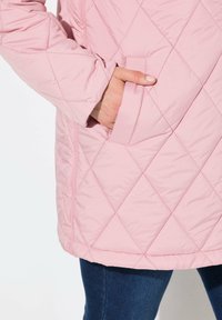 Chaqueta acolchada de color rosa claro con un patrón de diamantes, con un bolsillo lateral y una textura suave, combinada con denim oscuro.