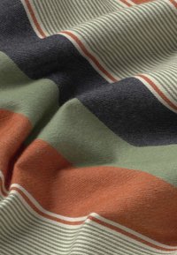 Tissu doux avec des rayures horizontales en vert olive, noir, orange brûlé et blanc, montrant la texture et des plis délicats.