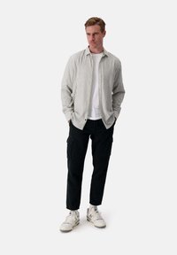 Camicia a righe verde chiaro e bianca, indossata sopra una maglietta bianca. Pantaloni cargo neri e sneaker bianche completano l'outfit.