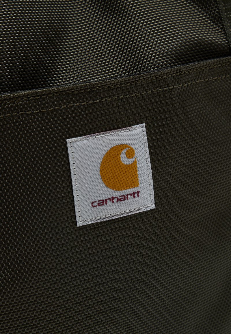 Close-up of dark textured fabric with a white Carhartt label featuring an orange logo stitched onto the surface.