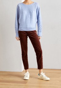 Jasnoniebieski sweter z dzianiny z diamentowym wzorem na klatce piersiowej, w połączeniu z brązowymi spodniami z sztruksu i białymi trampkami z turkusowymi akcentami.