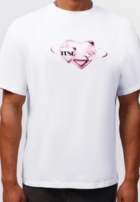 Hvid bomulds T-shirt med en pink hjertegrafik og ordet "FUSE" i sort, centreret på brystet. Korte ærmer, standard pasform.