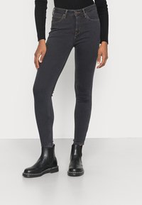 Jeans negros ajustados con cintura alta, que cuentan con cremallera y trabillas para cinturón, combinados con botas chelsea negras. Textura de denim suave.