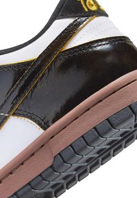 Svart lackläder sneakers med vita och gula detaljer, utrustade med en texturerad gummisula och noggrant sydda sömmar.