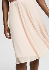 Lyserød nederdel lavet af gennemsigtigt stof, flydende design, knælang med lagdelt kant. Blød tekstur, uden synlige mønstre eller pynt.